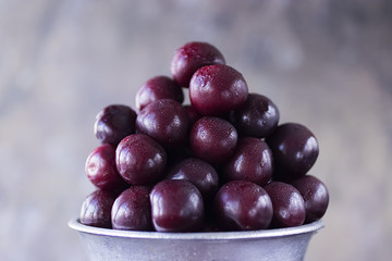 Ripe cherry in metal bucket on  dark wooden background.