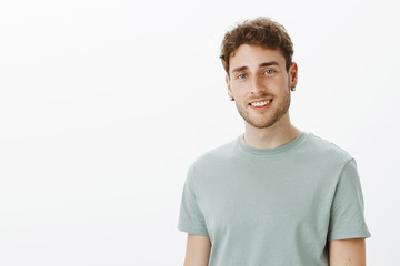 Obraz premium Indoor shot of cute fair-haired confident man with blue eyes and bristle, smiling broadly and gazing at camera, being in love with charming girlfriend, enjoying listening her talks over grey wall