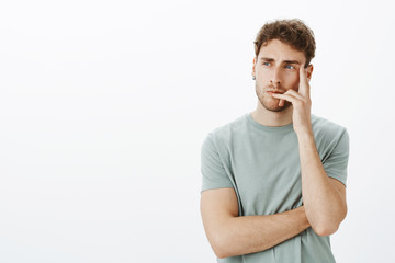 Portrait of focused smart and creative male model with short curly hair, holding fingers on lip and...