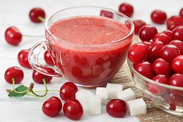 Natural cherry smoothie drink in glass cup with sugar and raw berries on white table