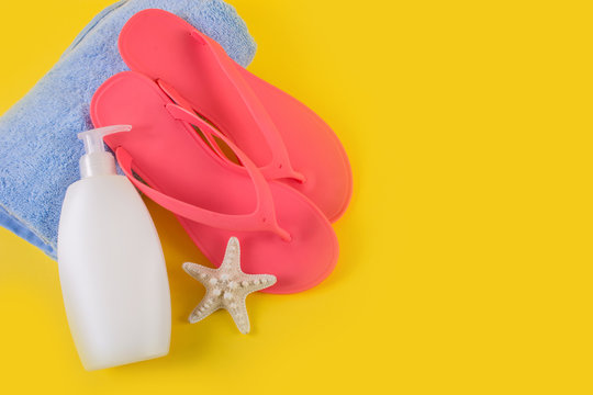 Pink sandal flip flop on blue towel and suntan cream lotion and starfish on yellow background. Summer vacations concept. Empty free space for text and design