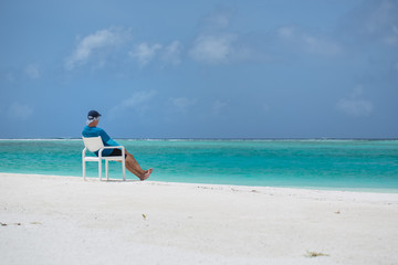 A man sits on a chair on the beach and looks out to sea