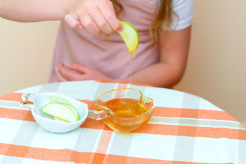 Close up of hands little girl eat apple with honey indoor. Jewish child dipping apple slices into honey on Rosh HaShanah the Jewish New Year.