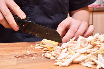 The man cook cuts roasted turkey meat on a cutting board with a knife. Close-up