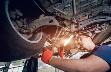 Car mechanic examining car suspension of lifted automobile at repair service station