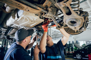 Car mechanics repair car suspension of lifted automobile at repair service station