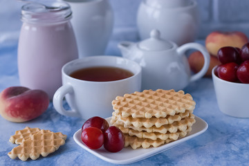 White cup of tea with thin waffles, yogurt and fresh cherry.