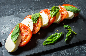 Caprese salad. Mozzarella cheese, tomatoes and basil herb leaves over stone table.