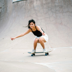 A portrait of a young and cool Chinese Asian skater girl playing with her skateboard. She enjoys skateboarding under the sun. © Danon