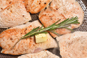 A branch of fragrant and fresh rosemary on roasted turkey meat in a frying pan. Close-up