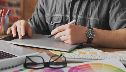 Young creative artist of web design in hat with graphic tablet in modern loft office