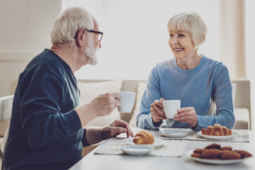 Positive mood. Joyful aged people smiling to each other while enjoying their meal