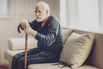 So depressed. Sad cheerless man holding a walking stick while thinking about his life