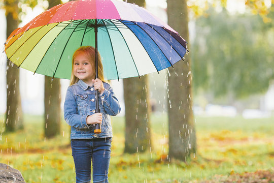 The image of a little girl with a rainbow umbrella in park