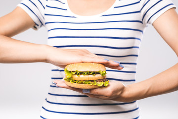 Young girl holding in female hands fast food burger, american unhealthy calories meal on white background, mockup space for text message or design.