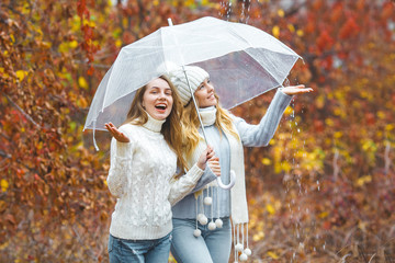 Young pretty girls having fun outdoors in autumn background. Cheerful friends in the fall time
