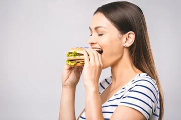 Fotobehang Young happy beautiful woman eating hamburger woman eating junk food, fatty food hamburger. White background, close-up, isolated. Diet concept. © denis_vermenko