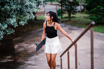 Obraz premium An image of a young and attractive Chinese Asian teenager wandering in the park while walking up the stairs. She is pretty, sporty, and she is carrying a skateboard with her.