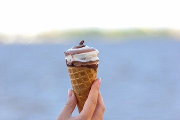 Ice cream cone, chocolate ice cream on blurred background, milk dessert on summer vacation, blank for designer with hand, copy space, milk product