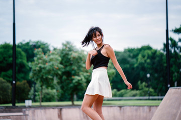 A portrait of a young Chinese Asian teenager in the skate park during the day. She is enjoying and smiling playfully as she whirls and twirls for a photograph.