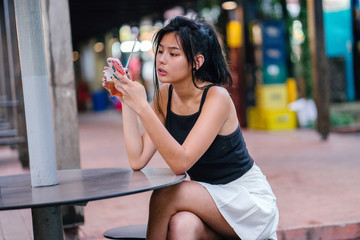 A trendy and fashionable Chinese Asian girl sitting at the hawker center while drinking her cold...