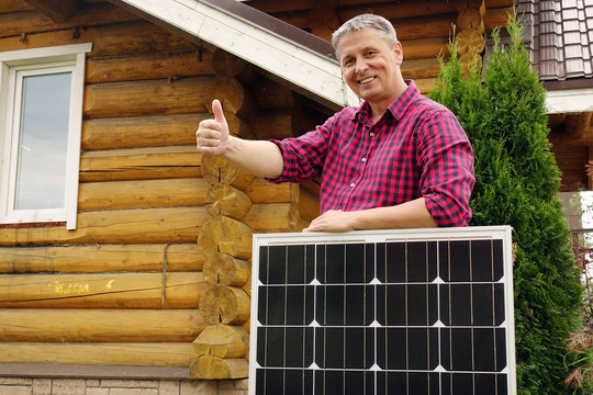 Solar panels in the hands of men . Energy production technologies. Wooden house background. The thumb of a person's hand upwards .