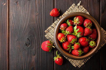 Fresh strawberries in ceramic bowl on dark wooden background