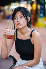 Portrait of a young Chinese Asian millennial girl sitting and enjoying a cold drink in a hawker...