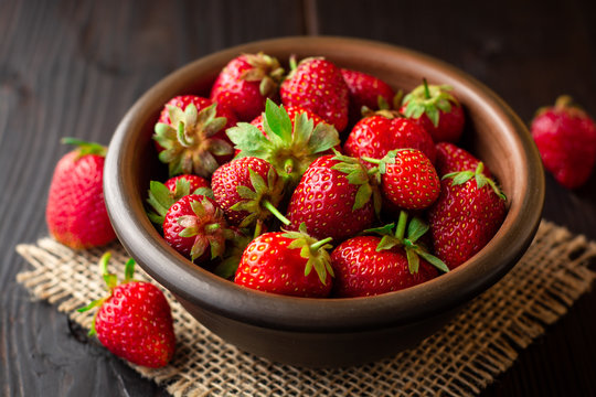 Fresh strawberries in ceramic bowl on dark wooden background