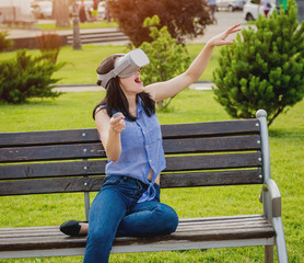 Naklejka premium A beautiful young girl plays a game wearing virtual reality glasses on the street.