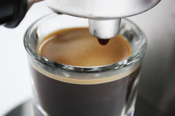 Espresso shot glass full of coffee with crema underneath an espresso machine