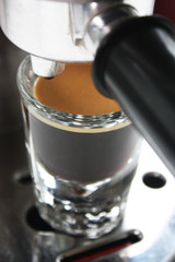 Espresso shot glass full of coffee with crema underneath an espresso machine