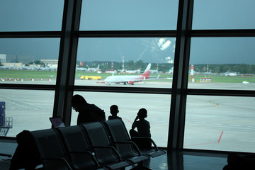 Silhouettes of family sitting at the window and looking at the airport strip with airplanes and...