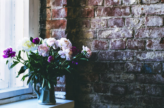Peonies on a window sill in loft style room with copy space on brick wall