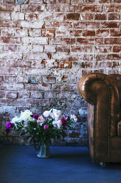 Loft interior details - leather sofa, bunch of flowers, brick wall and rough floor