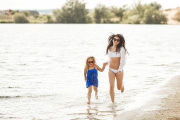 Mother and her little daughter having fun at the coast. Young pretty mom and her child playing near the water