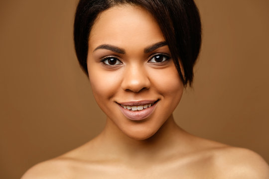 Beauty Portrait of attractive African American young woman with perfect skin and natural make up. Beautiful brunette model. Skin Face Care Concept. Looking on camera against brown background