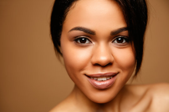 Close up Beauty Portrait of attractive African American young spa woman with perfect skin and natural make up. Beautiful brunette model. Skin Care Concept. Looking on camera against brown background
