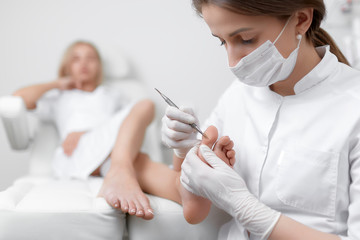 Podiatrist doctor caring about client foot with special iron tool.