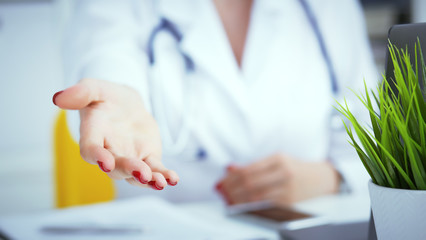 Female doctor making welcome gesture, politely inviting patient to sit down in medical office. Photo with depth of field.