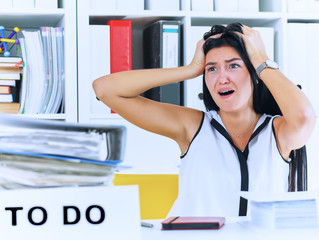 Young female office worker shocked by the huge amount of paper work. Deadline concepts.