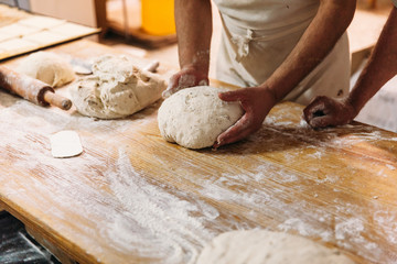 Baker is kneading dough to prepare bread on a rustic table in a bakery. Traditional Bakery Concept.