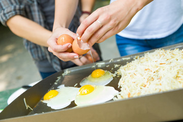 Young Adult Couple Cracking Open and Cooking Eggs and Potatoes At The Campground
