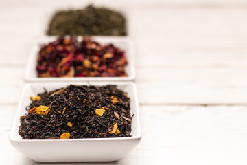 Close-up view of dry tea leaf in white scoops stand in row on white wooden table