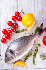 Fresh uncooked dorado or sea bream fish with lemon slices, spices, herbs and vegetables.