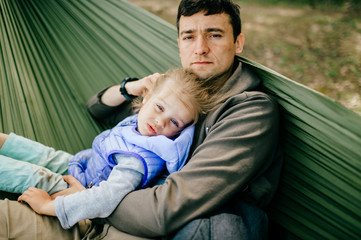 Modern Masculinity. Man in non-stereotypical role. Father caring his lovely daughter outdoor in summer.  Happy family expressing funny kind emotions at nature.  Parent with child leisure in hammock.