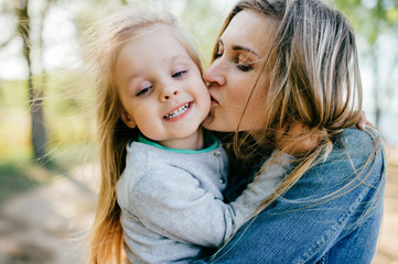 Happy smiling mother hugging her lovely little daughter outdoor. Lifestyle family. Adult cheerful...