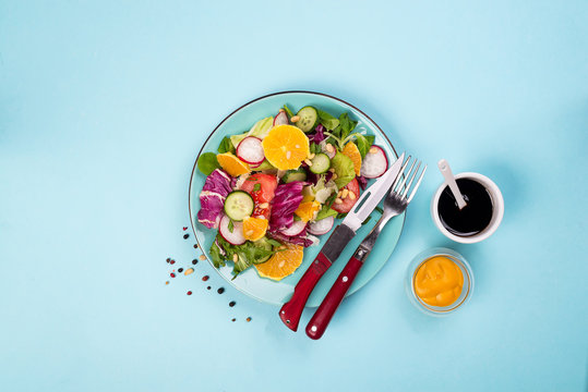 Fresh vegetables salad with various dressing on blue background, top view, border.