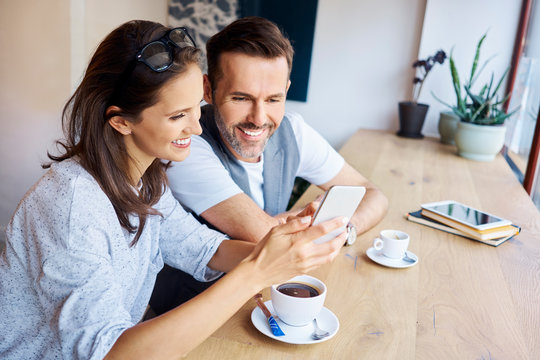 Couple looking at phone together while having coffee in cafe
