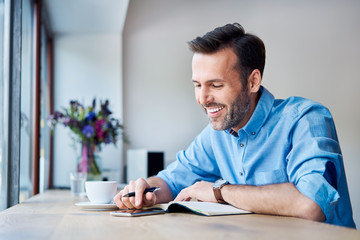Man looking at phone and writing in calendar while out for coffee in cafe
